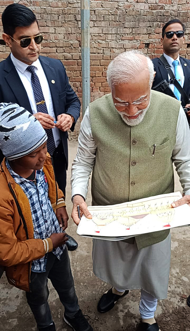 Prime Minister Narendra Modi looks at a drawing made by a boy standing next to him, in Ayodhya on Saturday.